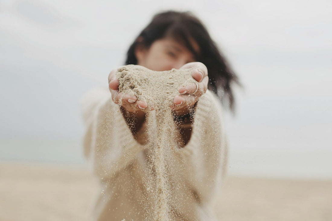 Woman with blurred face in soft sweater holding sand in her hands and letting it fall through her fingers, representing the process of emotionally letting go of someone you love after a breakup