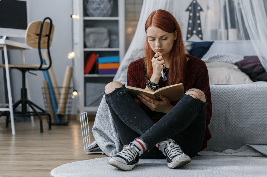 Woman sitting beside a bed and writing a goodbye message in a notebook while reflecting on someone she still loves.