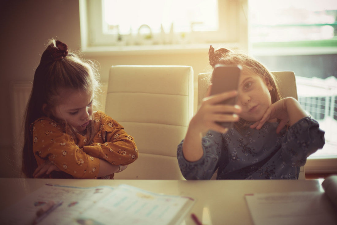 Retroactive jealousy concept illustrated through child checking phone while sibling shows jealous, withdrawn behavior