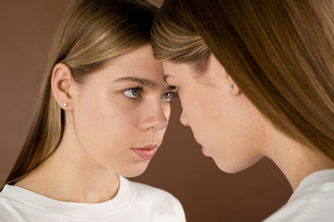 Woman experiencing jealousy and self-reflection after breakup, looking at her own reflection with contemplative expression
