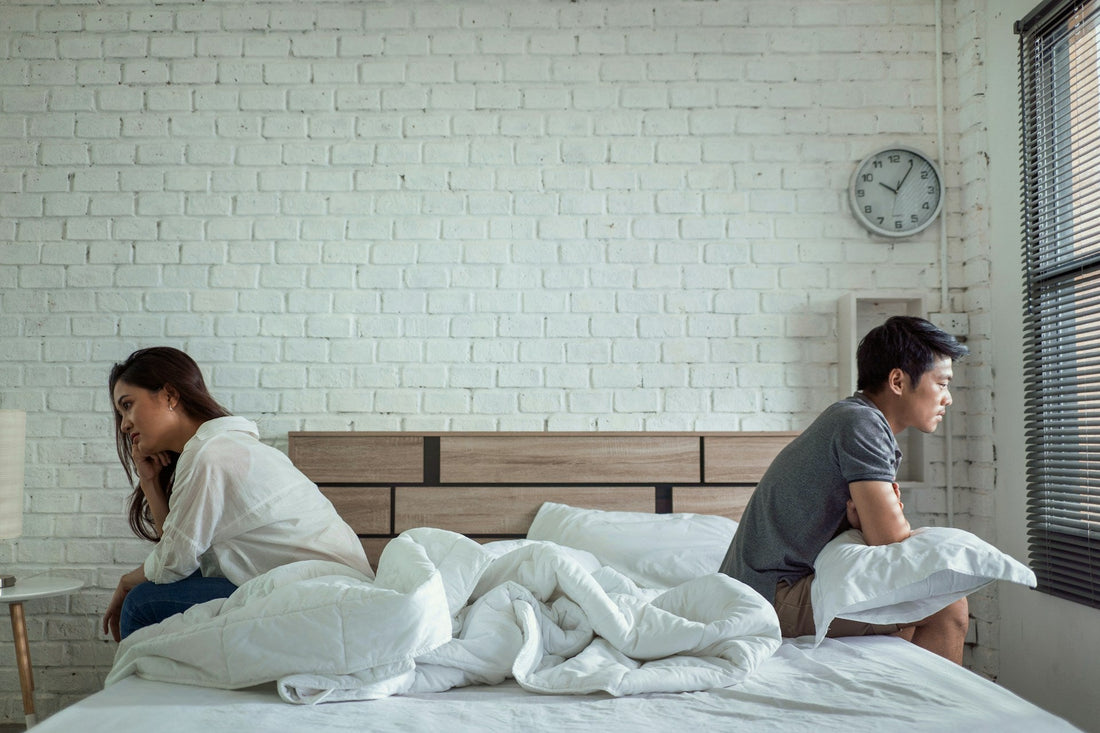 Couple sitting apart on opposite sides of a bed, showing ADHD-related emotional distance, relationship tension, and intimacy problems