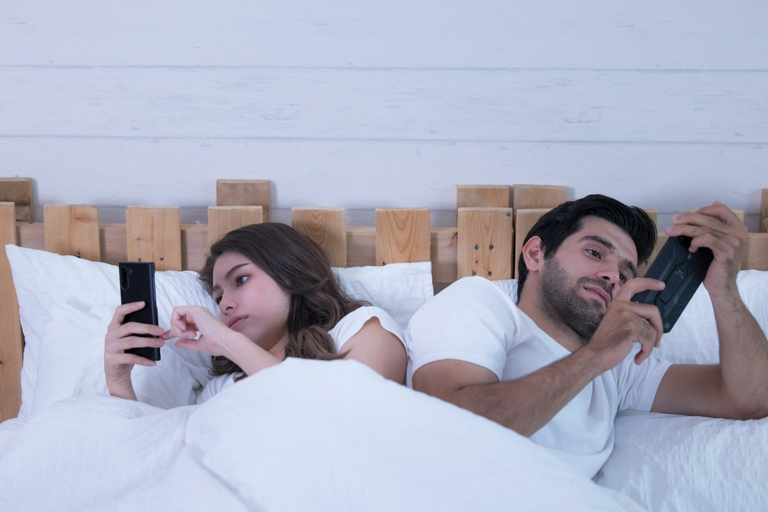 Couple lying apart in bed using separate devices, illustrating ADHD distraction, emotional distance, and reduced sexual intimacy