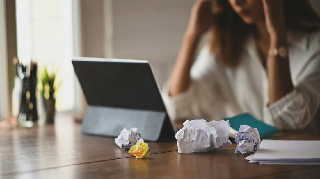 Overwhelmed woman at a desk with crumpled notes and a laptop, representing reminder fatigue and mental load in an ADHD relationship.