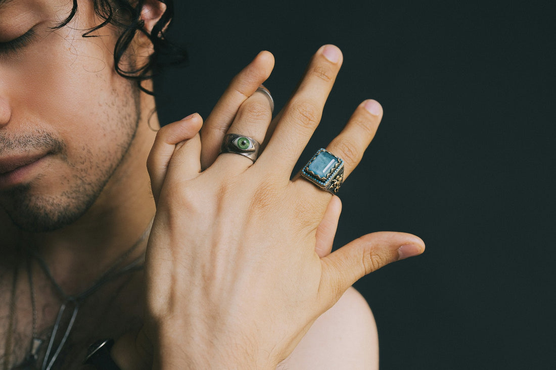 Man wearing two statement rings with blue and green stones, representing matching promise rings and coordinated couple jewelry styles