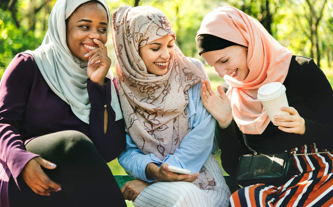 Three Muslim women looking at a smartphone together while discussing Muslim marriage apps and online matchmaking.