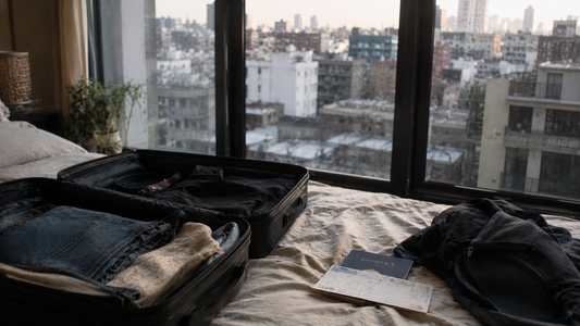 Half-packed suitcase on a bed beside a passport and travel ticket, overlooking a city skyline through an apartment window, symbolizing the difficult decision of relocating for a relationship and closing the distance between partners.