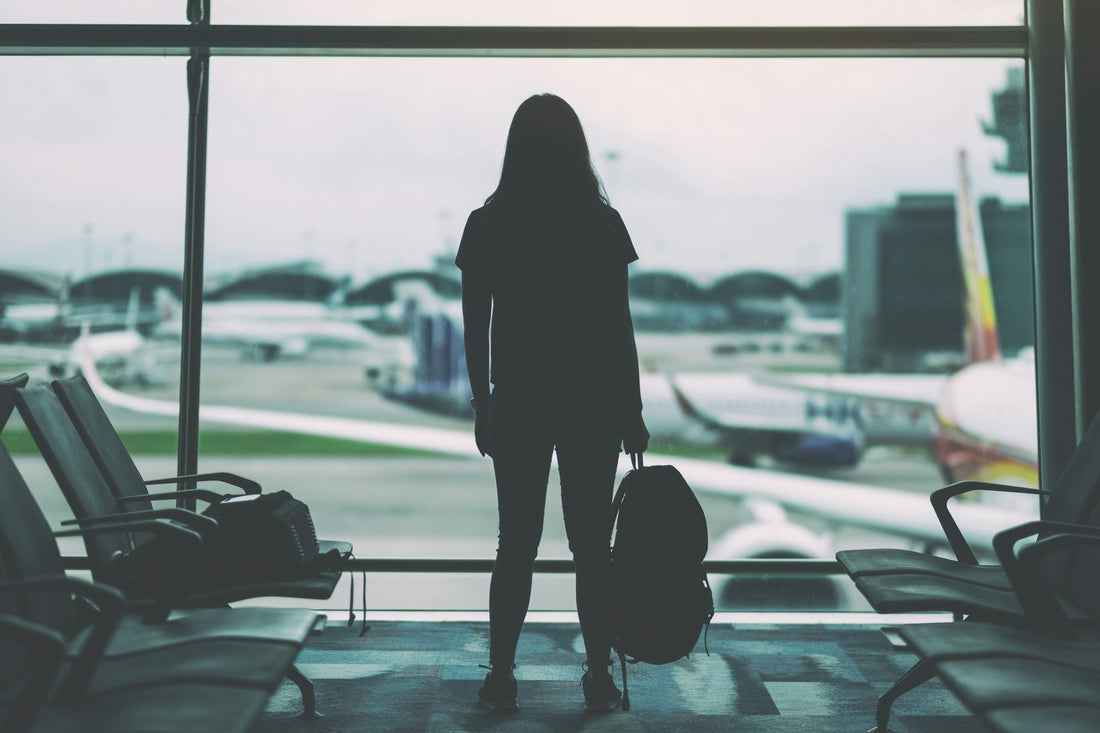 Person standing alone at an airport with luggage, representing a long-distance breakup where both partners may still love each other.