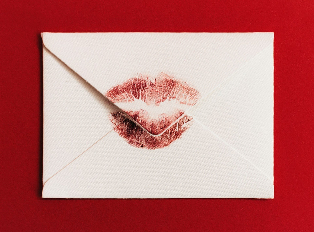 A white textured envelope with a breakup letter inside and a red lipstick kiss mark on the front, set against a solid red background.