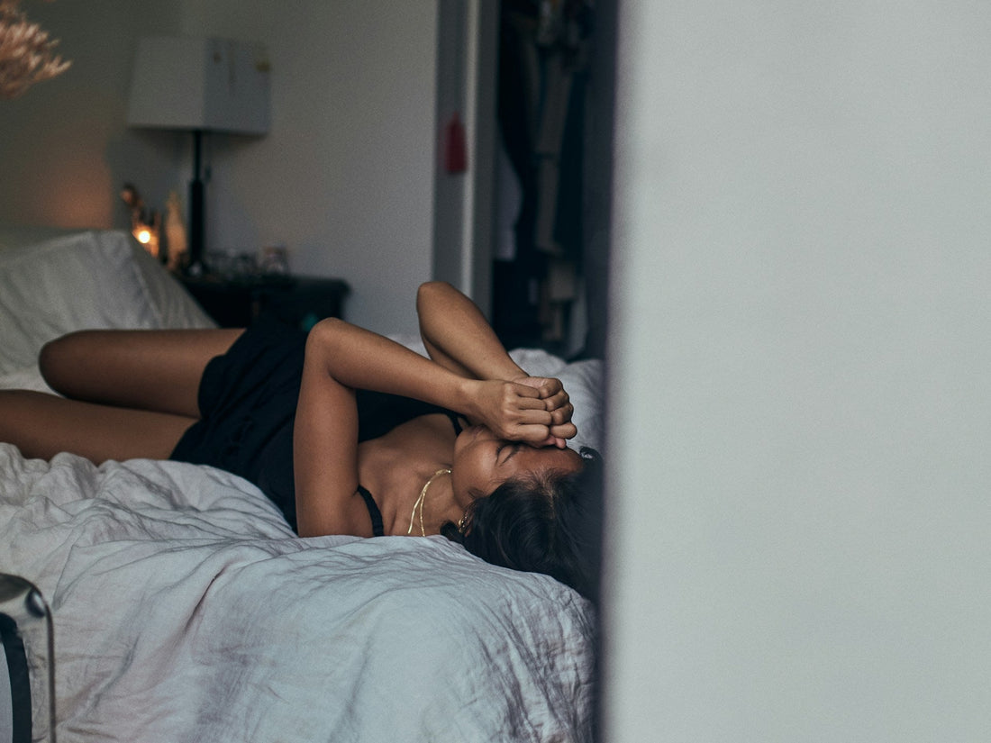 Exhausted woman lying on a bed with her hands over her face as stress, fatigue, and mental overload reduce sexual desire