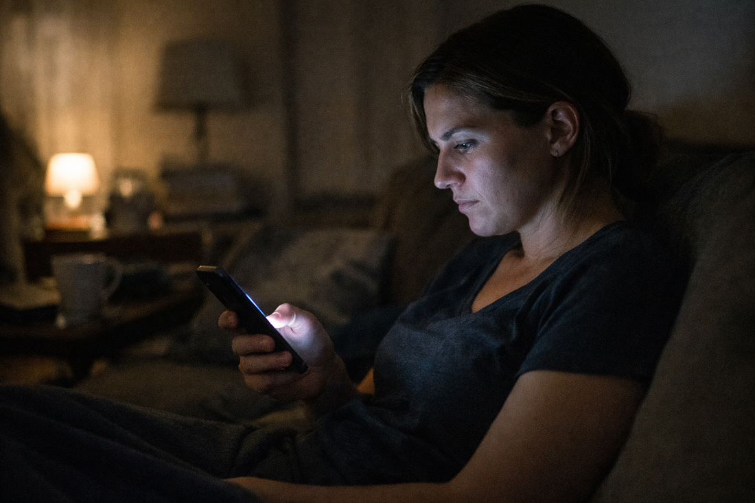 person quietly scrolling on their phone at night with a tense expression