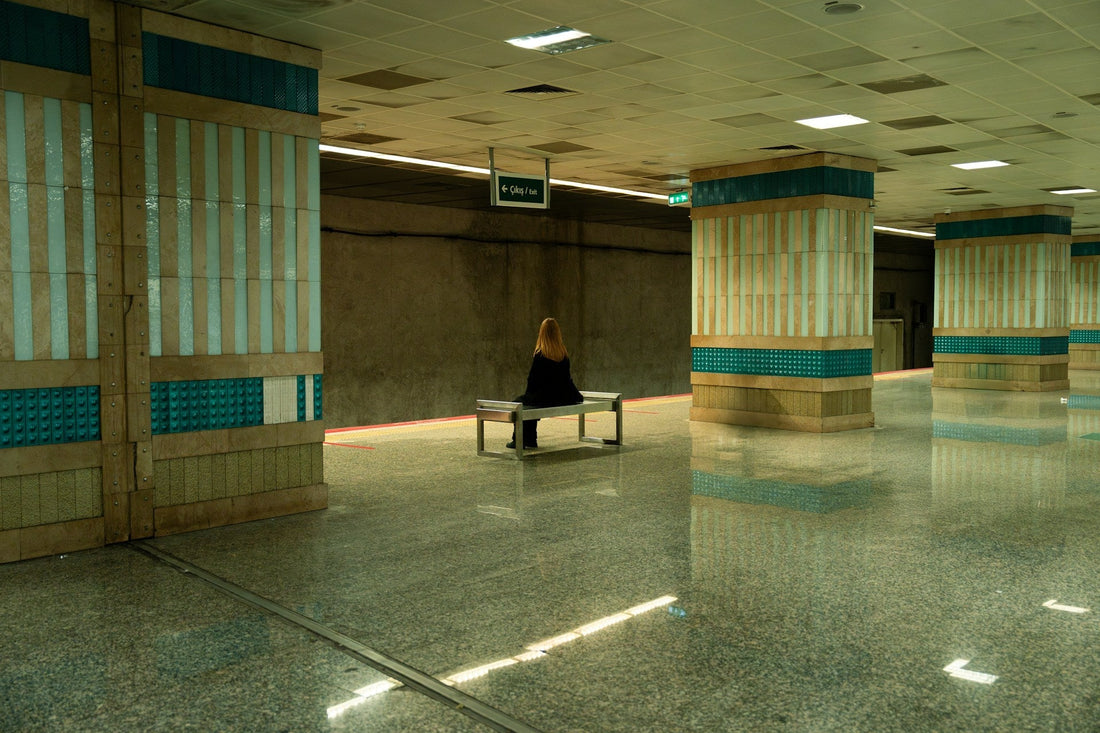 Woman sitting alone on a bench in an empty train station after a breakup, reflecting emotional distance and moving on.