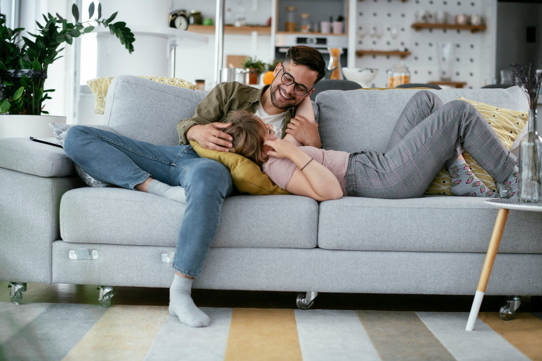 Couple cuddling closely on a sofa at home, representing emotional intimacy, physical affection and feeling safe, connected and comfortable in a relationship.
