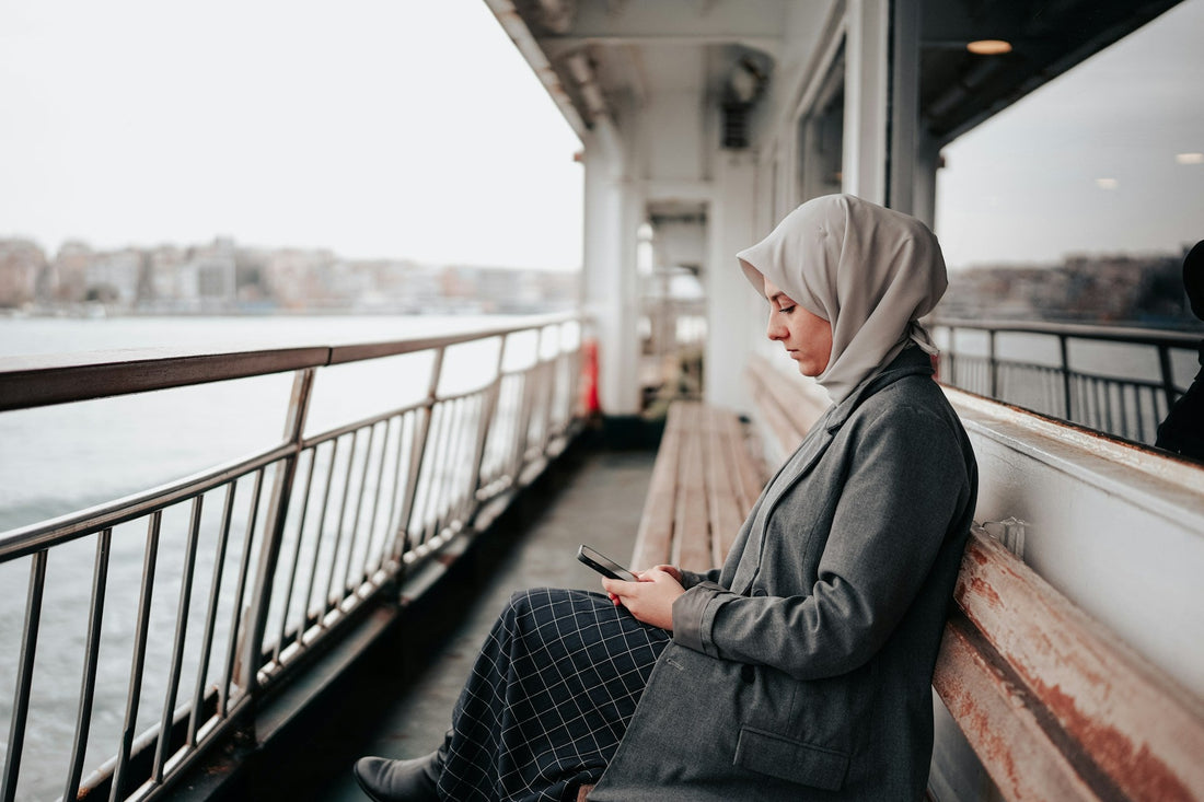 Muslim woman sitting alone with her phone after ending a haram relationship, representing attachment withdrawal, no contact and emotional recovery.