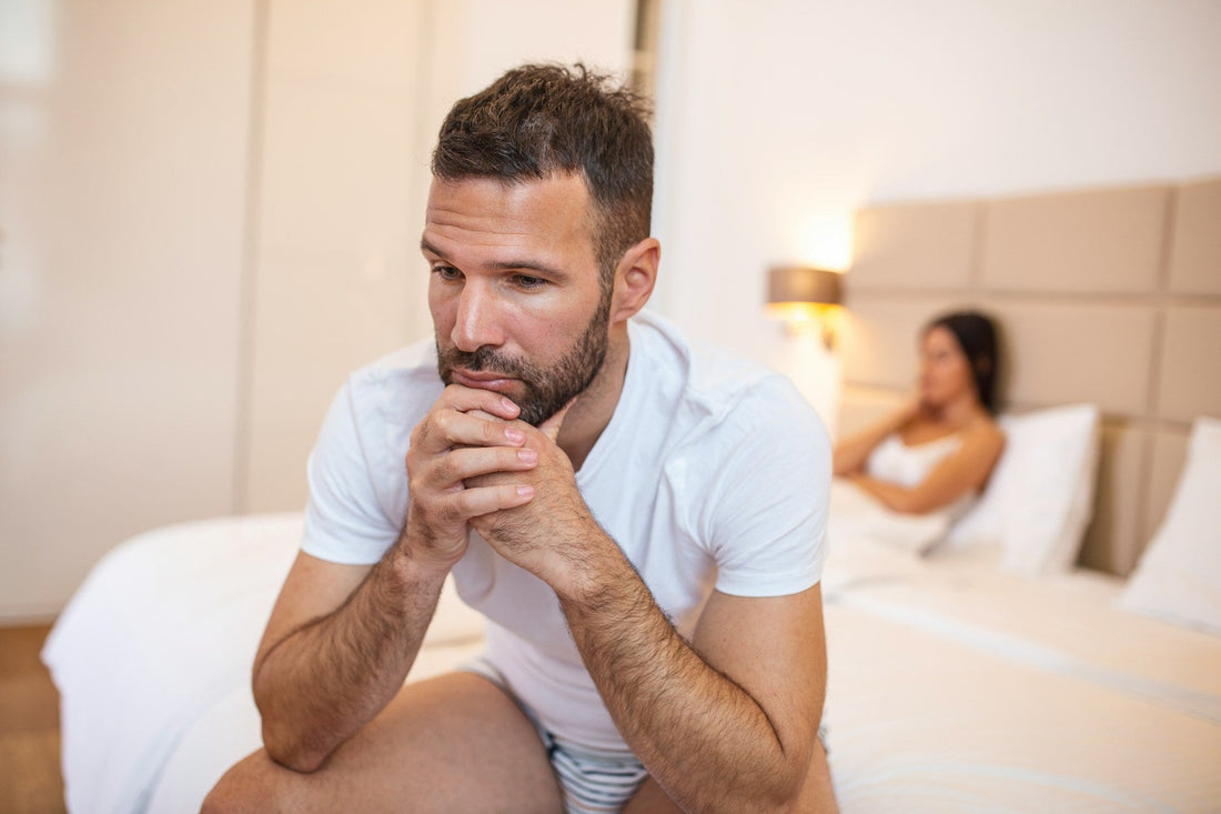 Man sitting apart from his partner and looking conflicted, representing fear of commitment, relationship anxiety and emotional withdrawal as a relationship becomes more serious.