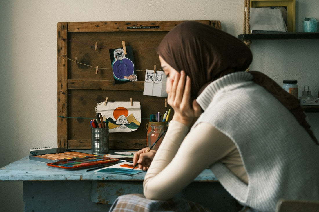 Muslim woman sitting thoughtfully at an art desk while healing emotionally after a broken engagement in Islam.