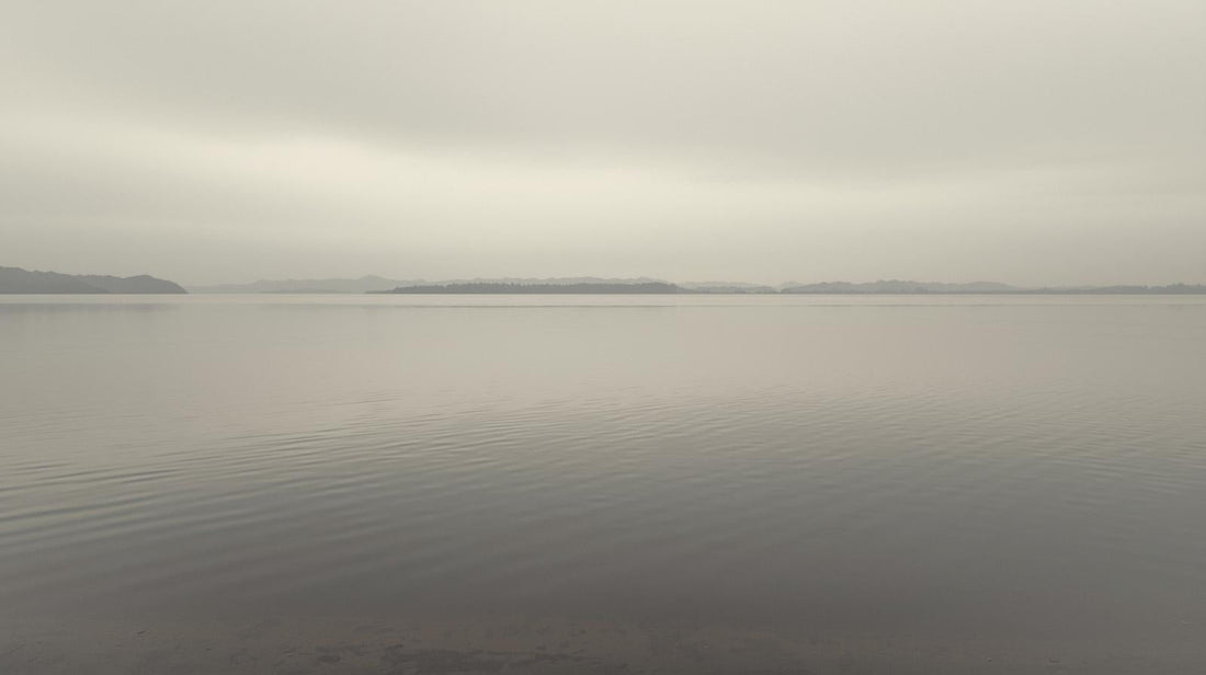 Smooth lake surface under soft overcast light with no ripples, symbolizing calm stability that may feel boring compared to emotional intensity
