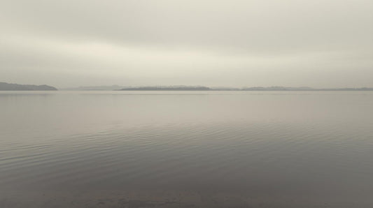 Smooth lake surface under soft overcast light with no ripples, symbolizing calm stability that may feel boring compared to emotional intensity