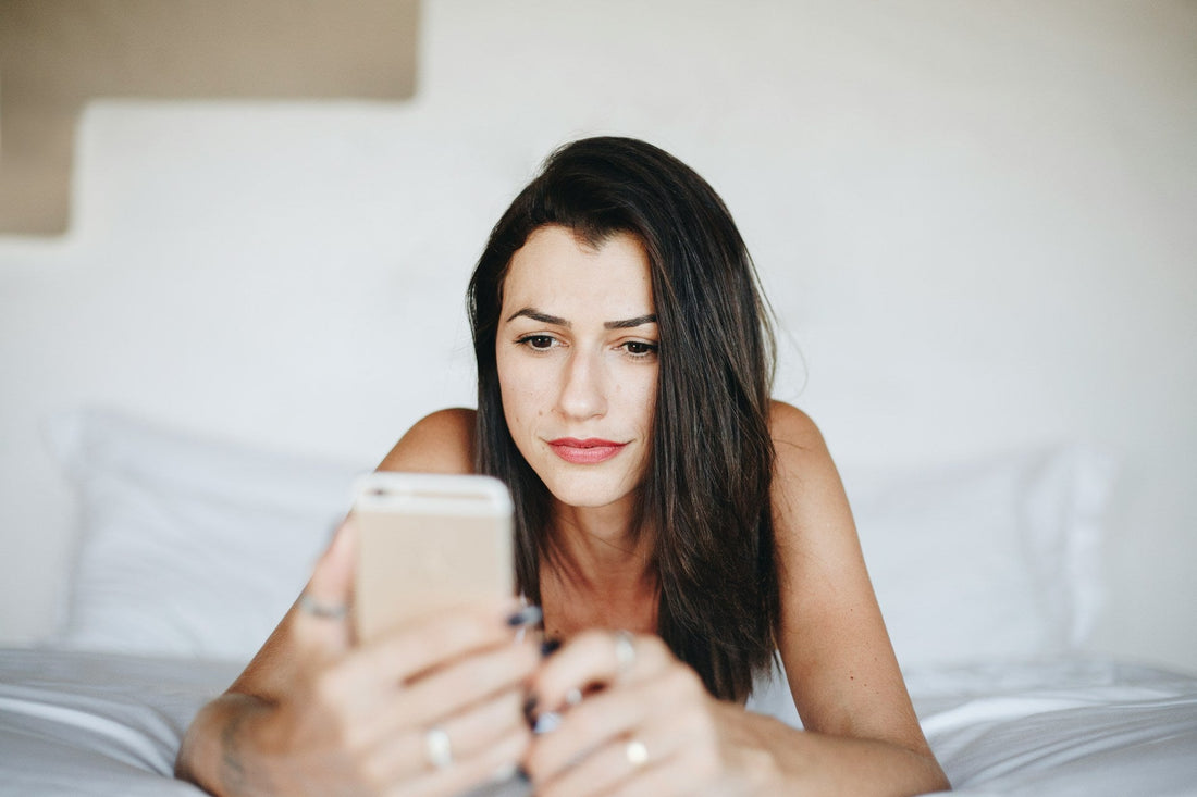 Woman lying on a bed checking her phone, representing waiting for clarity in a situationship