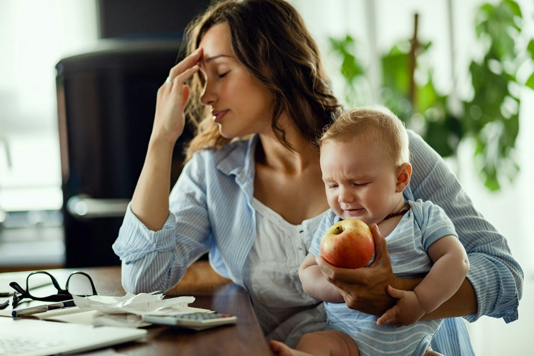 Stressed mother reviewing household bills while holding her baby, representing financial dependency and limited independence in a controlling relationship.