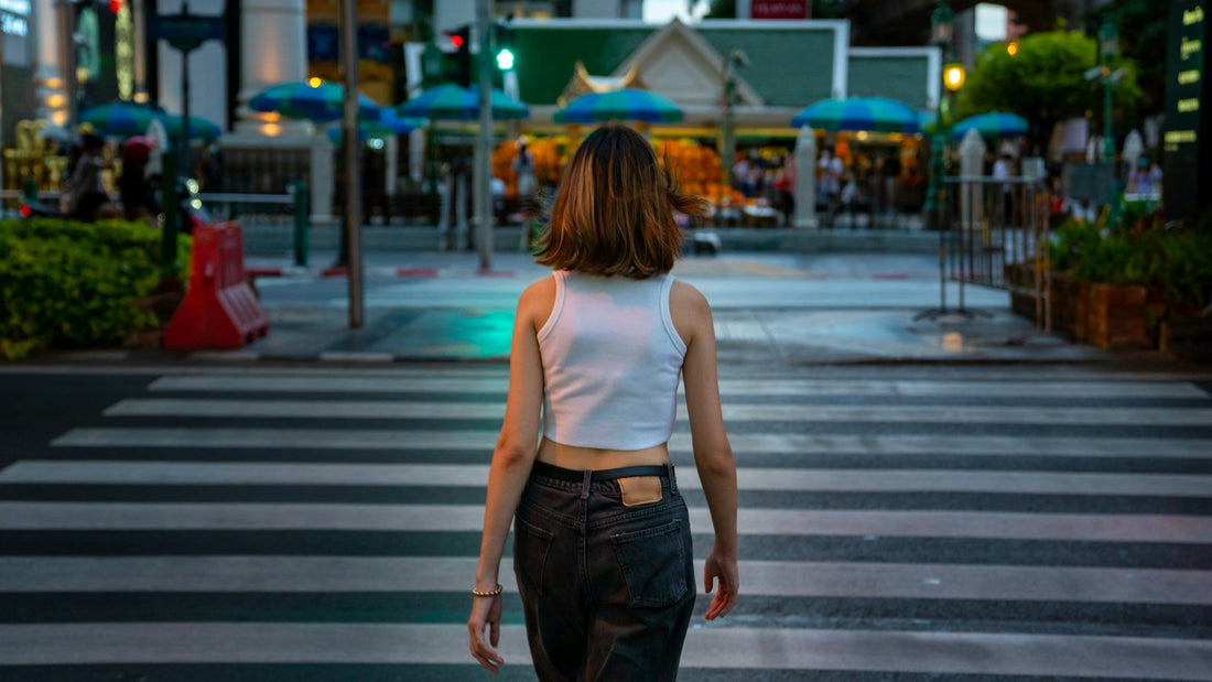 A woman in a white tank top and dark jeans walking across a crosswalk symbolizing someone building a new life after relationship