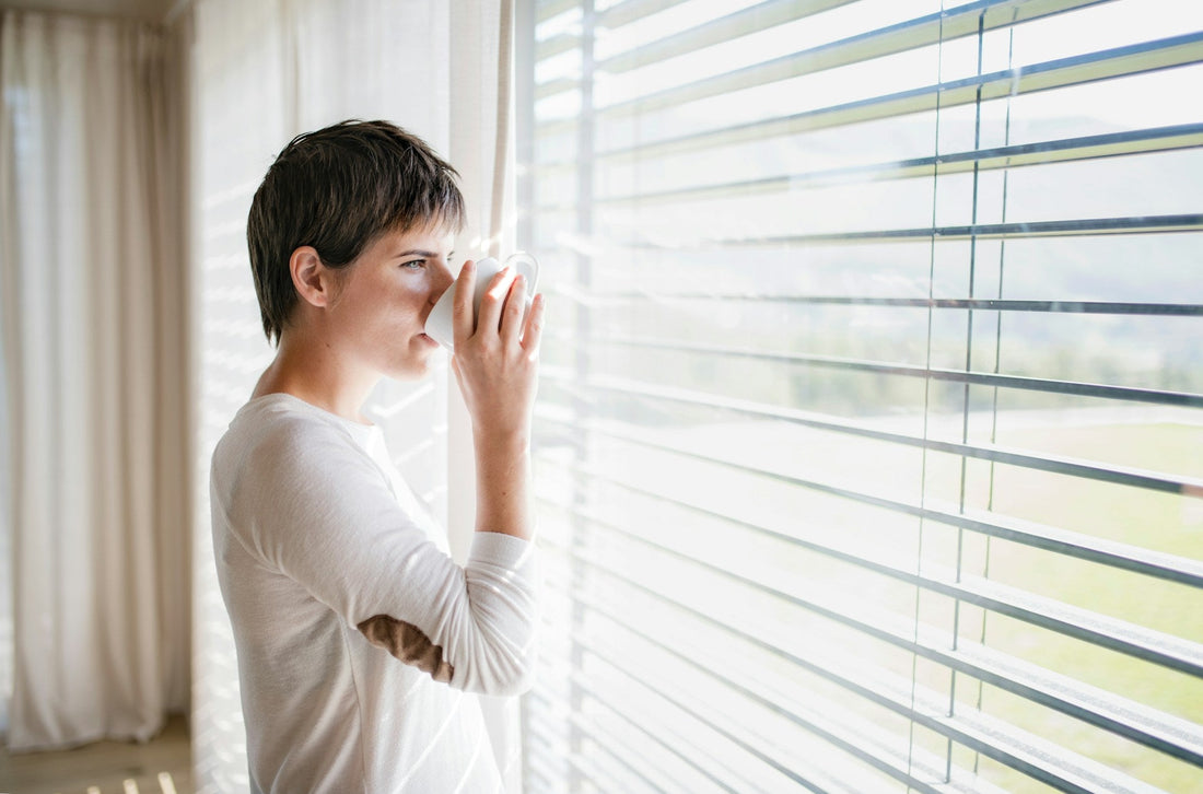 Woman drinking from a mug while looking out a bright window, representing reflection and moving on after a situationship