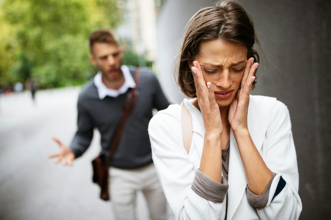 Distressed woman covering her face while her partner argues behind her during a disrespectful relationship conflict