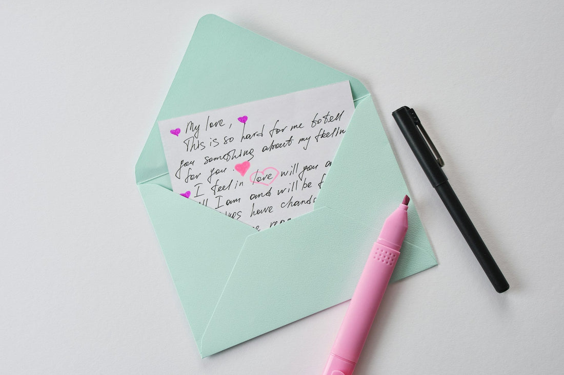 A mint green envelope on a white surface with a handwritten breakup letter not intended to send tucked inside, alongside a pink highlighter and a black pen.