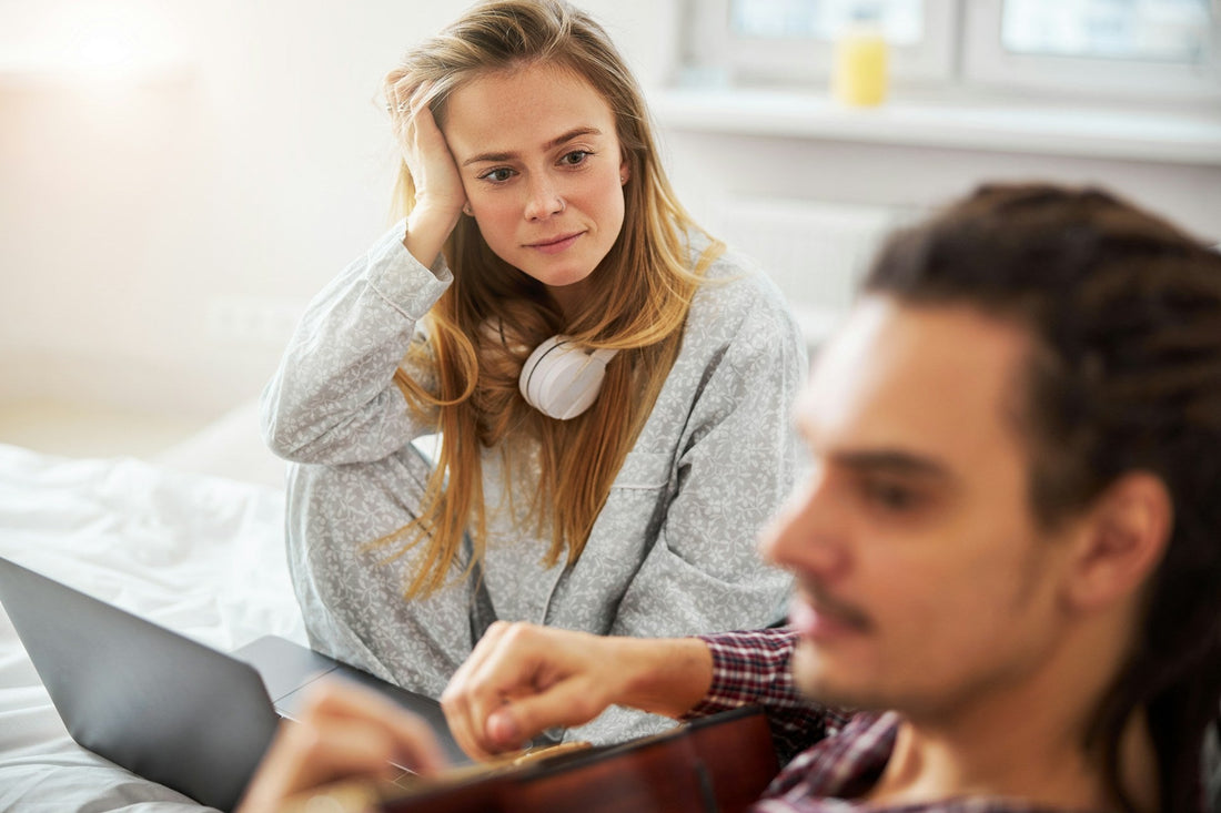 Woman looking toward her distracted partner while sitting together at home, representing feeling unimportant, overlooked and emotionally deprioritised in a relationship.