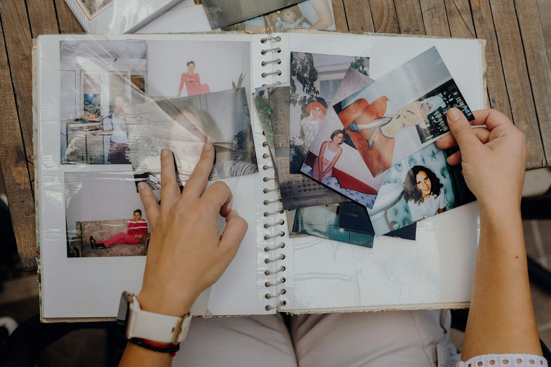 A person's hands holding and turning pages of a spiral-bound photo album filled with printed photographs, set on a wooden surface.