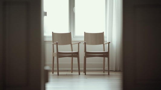 Two chairs angled slightly away from each other near a window representing emotional tension and jealousy