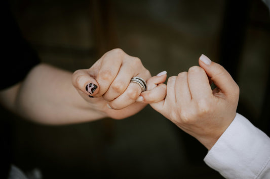 Couple linking pinkies while wearing rings, representing the promise behind a commitment ring and how much promise rings cost