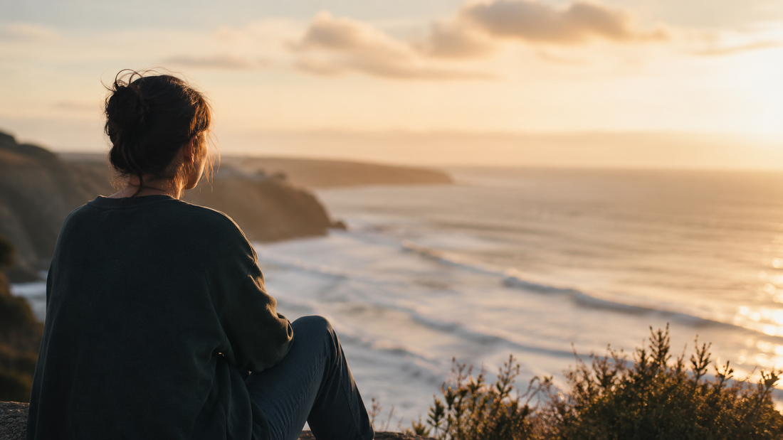 Woman sitting alone by the sea at sunset, reflecting on letting go after a breakup and moving forward without pretending it did not matter
