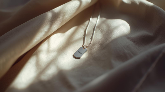 Minimal dog tag necklace resting on neutral linen in soft natural light symbolizing connection across distance