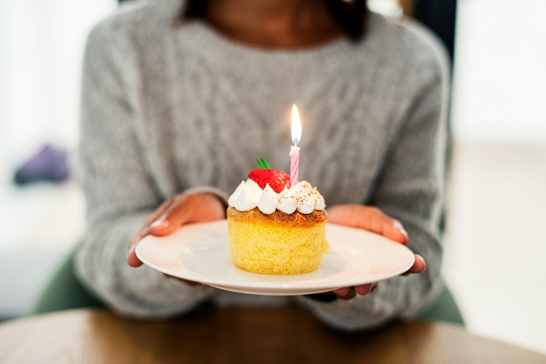 Long distance couple celebrating birthday over video call with cake candles and gift in warm evening setting