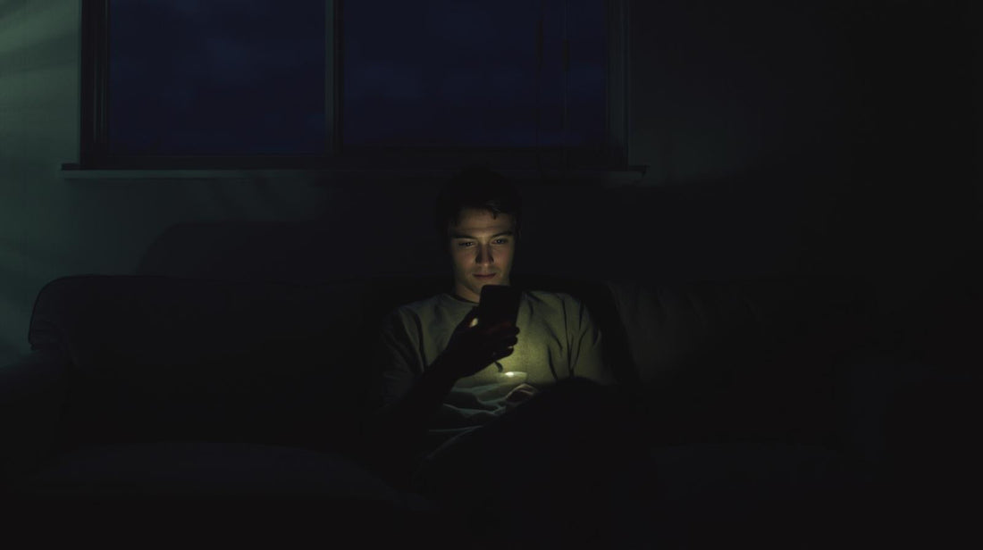 Person sitting alone holding phone in dim room, symbolizing insecurity in a long distance relationship