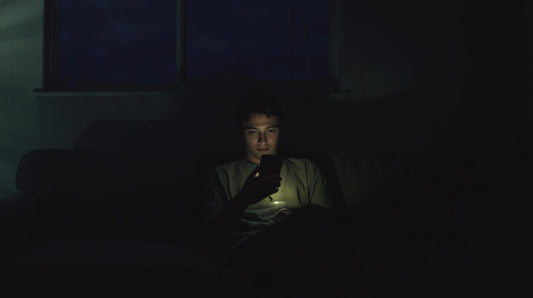 Person sitting alone holding phone in dim room, symbolizing insecurity in a long distance relationship
