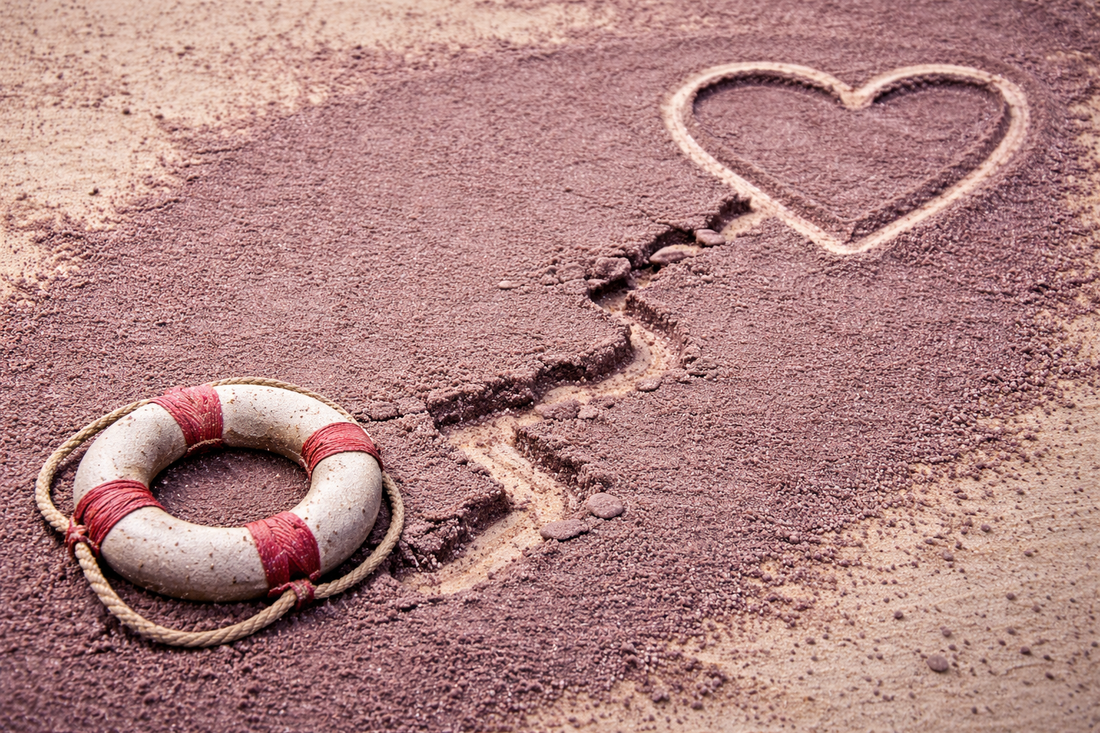 Heart drawn in sand separated by a crack with a life ring nearby symbolizing loving someone from a distance while allowing consequences