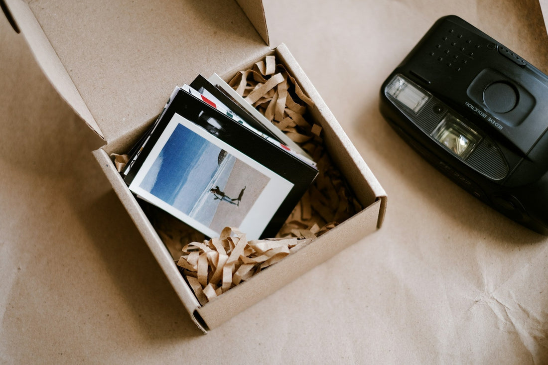 Open cardboard memory box filled with printed photographs beside a camera, symbolising preserving memories while letting a same-sex relationship end.