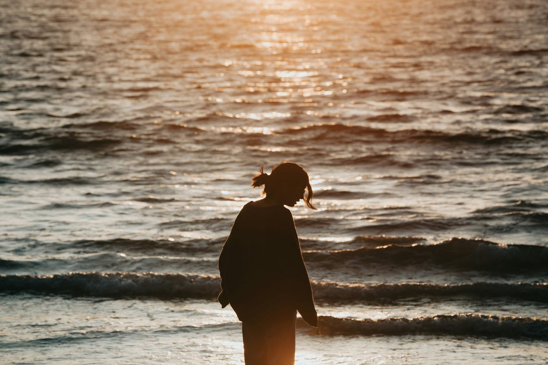 Silhouette of a person standing alone by the ocean at sunset, representing the loneliness and contemplation of whether to reach out to an ex after a breakup