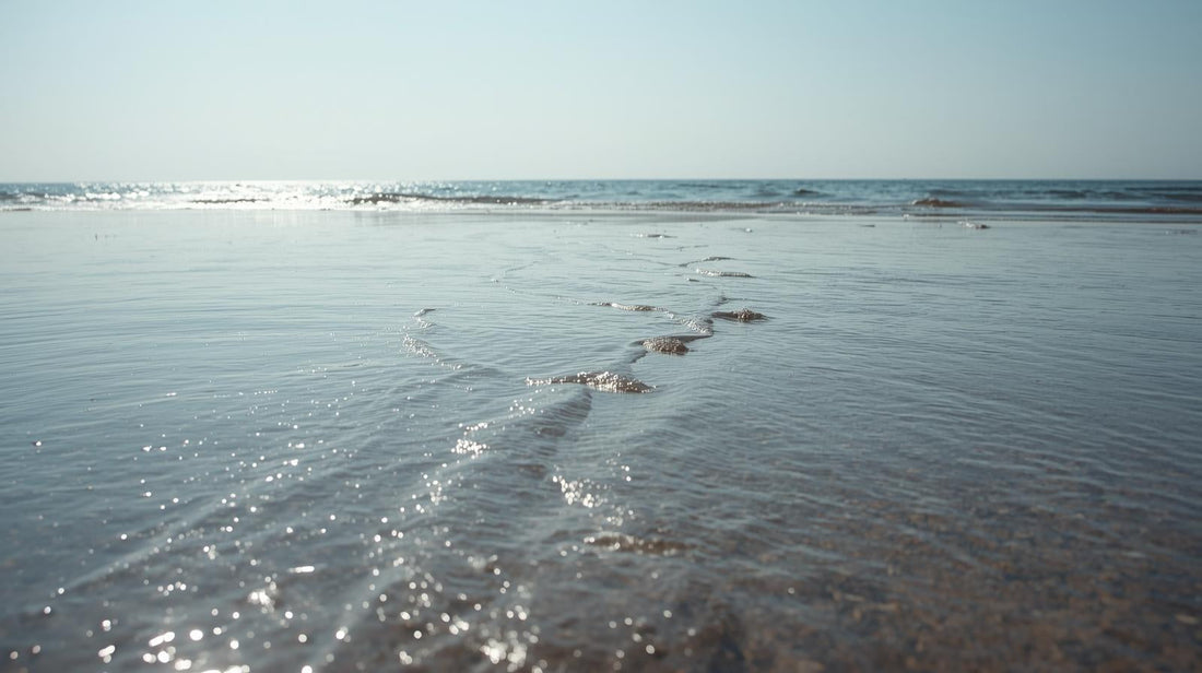 Calm shoreline at low tide with gentle waves approaching reflective wet sand, symbolizing how missing someone returns in emotional waves over time
