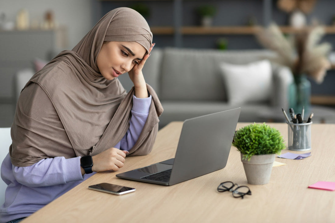 Muslim woman sitting alone at a desk looking distressed after a breakup, representing guilt, regret and emotional recovery.
