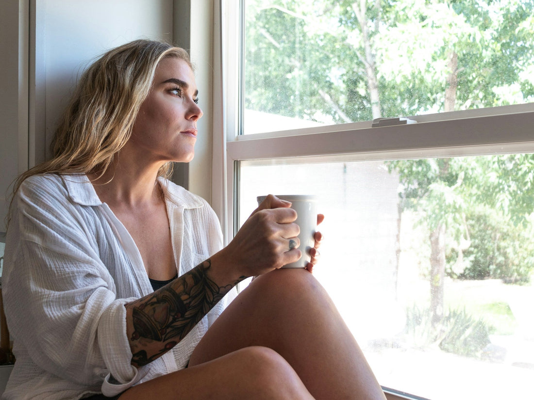 Woman sitting by a window with a mug, reflecting during no contact after a situationship