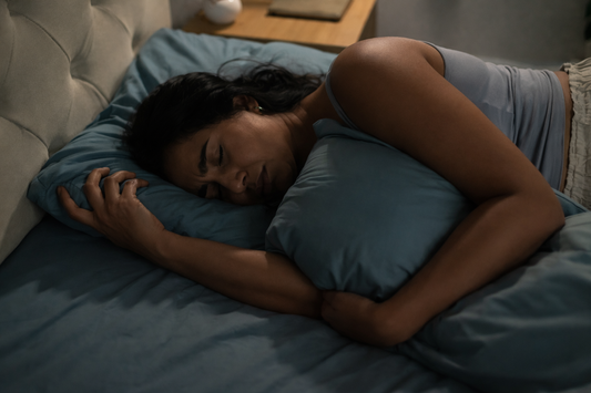 Woman lying on her side in bed at night, holding a pillow close while resting in quiet, unresolved thought.