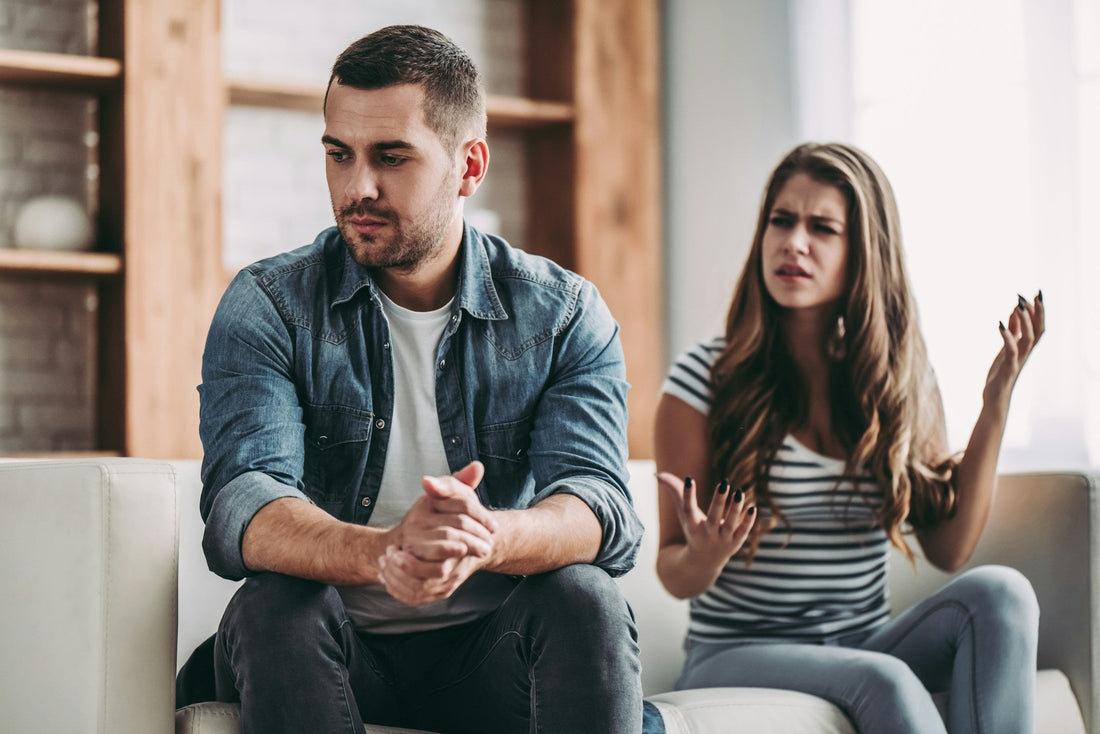 Man sitting withdrawn while his partner speaks to him, representing commitment issues, emotional distancing and difficulty moving a relationship forward.