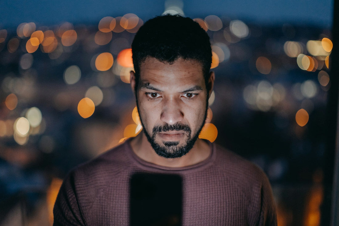 Man looking intently at his phone at night, representing monitoring, jealousy and controlling behaviour in a relationship.
