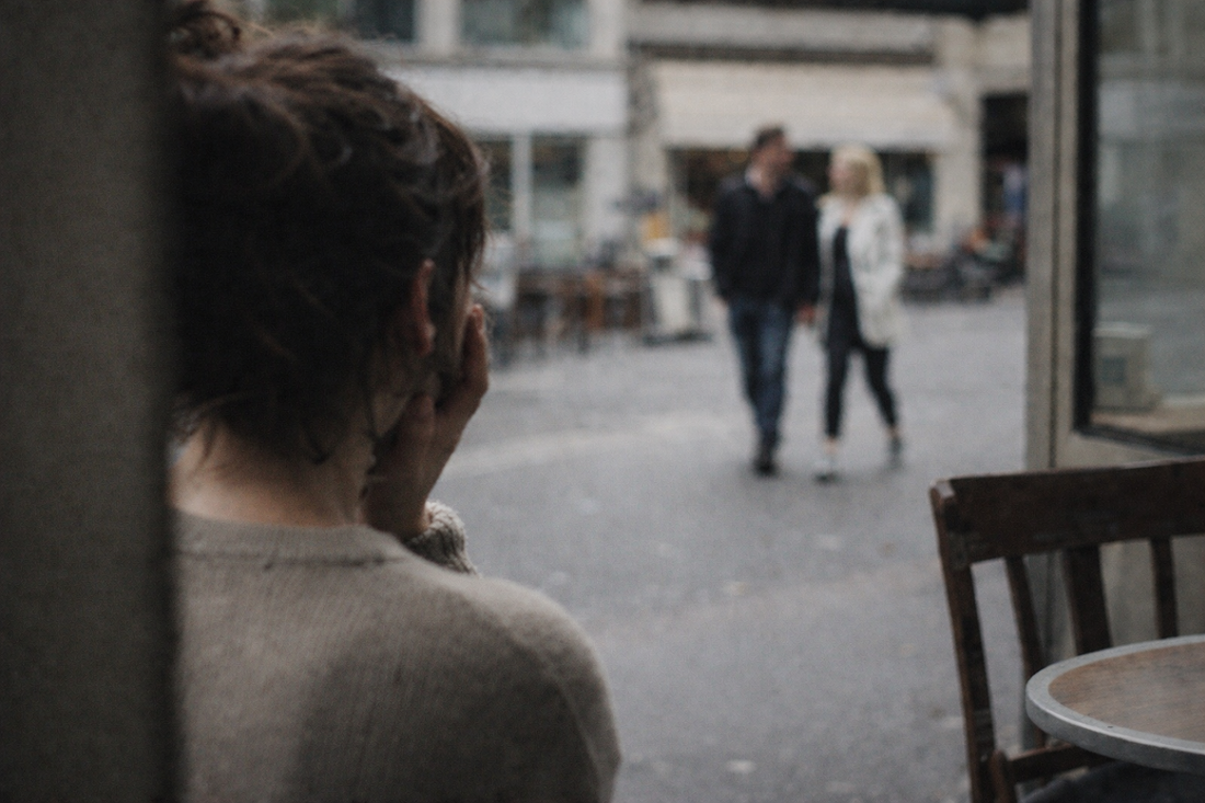 Woman watching her ex walk with a new partner while comparing herself from a distance