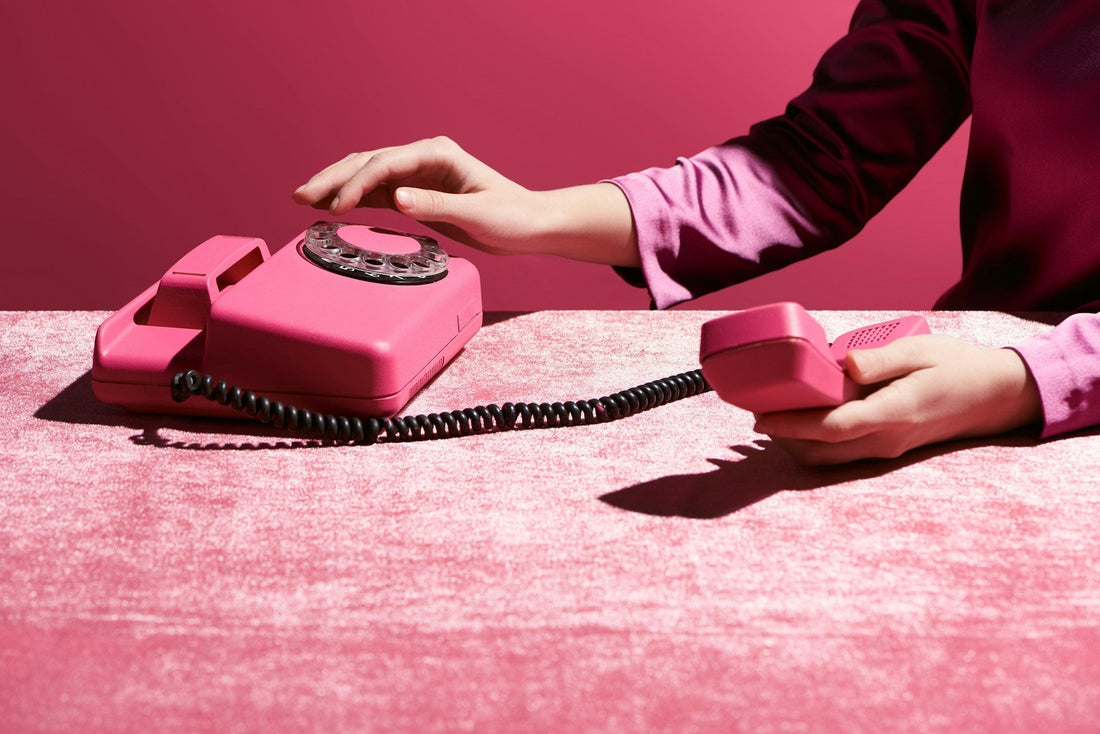 A hand reaching toward a pink rotary phone, symbolizing the urge to call an ex after a breakup.