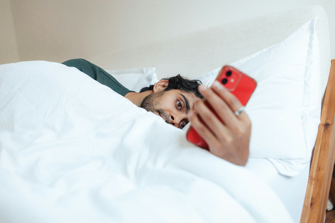 Man lying in bed looking at his phone, representing uncertainty and mixed signals in a situationship