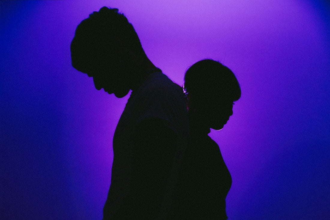 **SEO alt text:** `Silhouetted couple standing back to back against purple light, representing uncertainty between a situationship and a committed relationship`