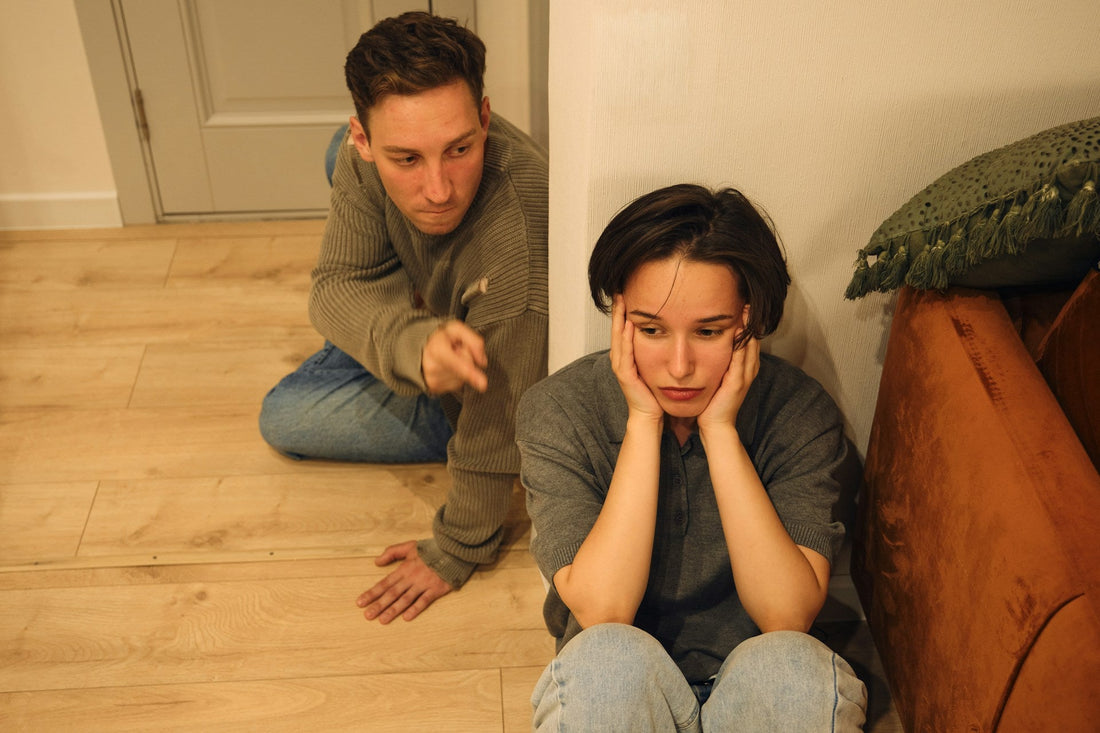 Emotionally exhausted woman sitting apart while her partner continues arguing and pointing during a painful relationship conflict